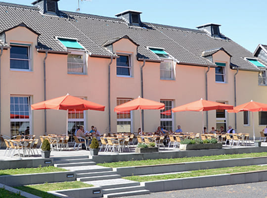 Frontalansicht des Außenbereichs der Klostertube mit schöner Außengarnitur und großen aufgespannten Sonnenschirmen