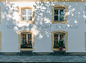 Eindrucksvolle Fassade der Schlosswirtschaft Schwaige mit beschmückten Fenstern und einer modernen gemalten Aufschrift