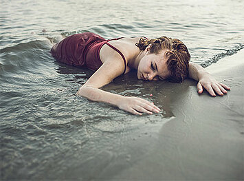 Eine Frau in einem roten Kleid liegt bewusstlos im Meer