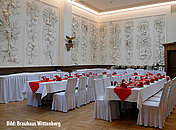 Großer Speisesaal mit antik gestalteter Wand, hoher Fensterdecke und liebevoll angerichteten Tischentafeln