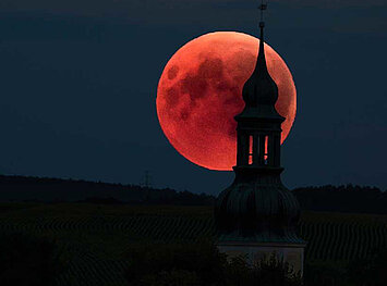 Ein rot leuchtender Mond scheint durch den Kirchturm