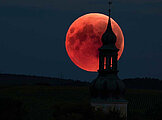 Ein rot leuchtender Mond scheint durch den Kirchturm