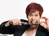 Eine rothaarige Dame hält ein scharfes Messer zwischen den Zähnen
