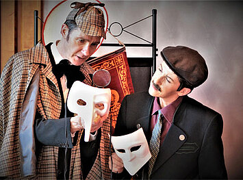 Sherlock Holmes und Dr. Watson halten jeweils eine weiße Maske in der Hand.