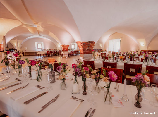 heller Gewölbekeller mit festlich gedeckten Tafeln und Blumenvasen