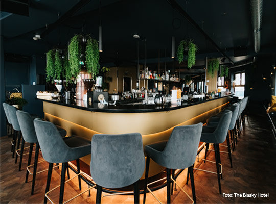 dezent beleuchtete Bar mit samtbezogenen Barhockern