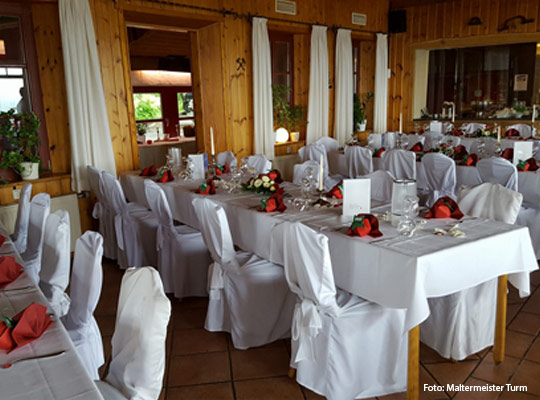 festlich gedeckter Gastraum mit weißen Stuhlhussen und Holzwänden