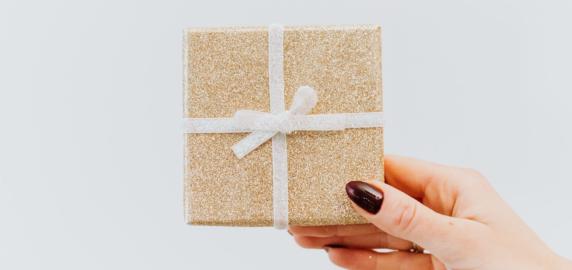 Schön eingepacktes Geschenk in goldenem Geschenkpapier mit weißer, gebundener Schleife wird von einer Hand hochgehalten