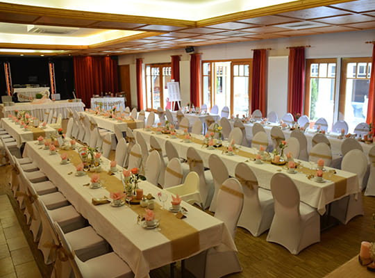 Großer Festsaal mit langen, weiß dekorieren Tischtafeln inklusive Bühne, angerichtet für das Dinnerkrimi