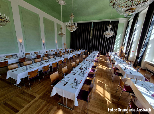 Saal mit großen Fenstern und stilvoll gedeckten langen Tafeln