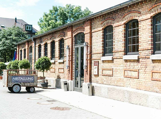 Blick auf die sonnenbestrahlte Außenfassade des Backsteinhauses. Zudem steht ein alter Anhänger vor dem Restaurant.