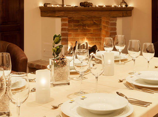 Ein für das Dinnerkrimi gedeckter Tisch, in weißer Farbe gehalten. Im Hintergrund ein befeuerter Kamin.