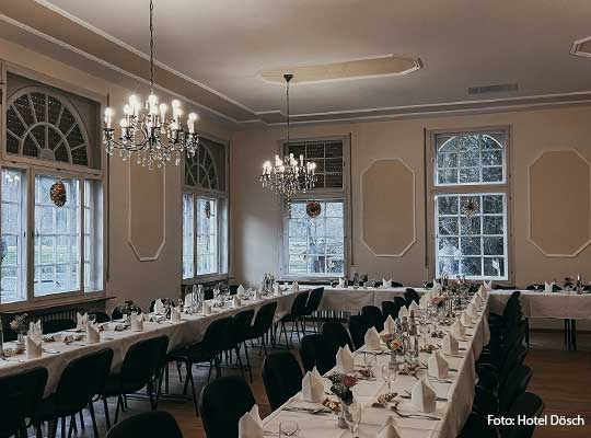 Großer Raum mit Kronleuchtern und einer langen U-Tafel