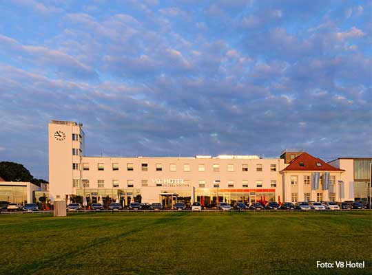 Grüne Wiese vor dem sonnenbestrahlten V8 Gebäude.