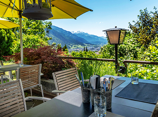 Gemütliche Terrassenmöbel im Außenbereich des Restaurants kombiniert mit einem eindrucksvollen Ausblick auf die Berge.