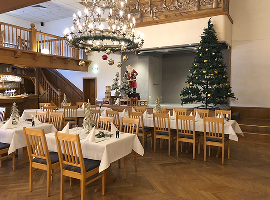 Auf der Bühne des Saales steht ein großer Weihnachtsmann, die Tische dekoriert für eine unvergessliche Weihnachtsfeier mit unserem Dinnerkrimi Dortmund.