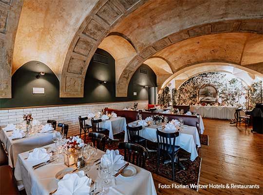 lange Tischtafeln im riesigen Speisesaal mit steinernen Rundbogendecken und schöner Beleuchtung.