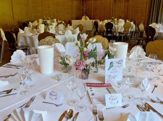 Schön eingedeckter Tisch mit Blumengestecken und weißen Tischdecken und Stoffservietten, liebevoll drapiert mit edlem Geschirr auf einem Rundtisch 