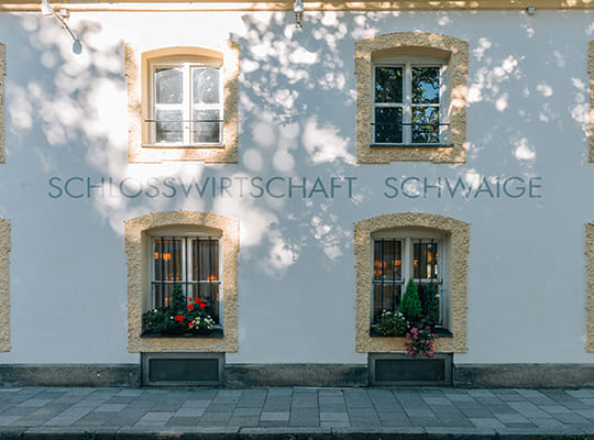 Eindrucksvolle Fassade der Schlosswirtschaft Schwaige mit beschmückten Fenstern und einer modernen gemalten Aufschrift