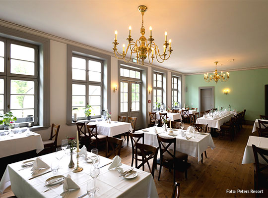 Langer Raum mit festlich gedeckten Tischen, an der Decke ist ein Kronleuchter zu sehen.