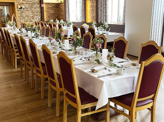 Gemütlicher Speiseraum mit langer Tafel, welche schön angerichtet ist mit weißer Tischdecke und tollen Blumengestecken