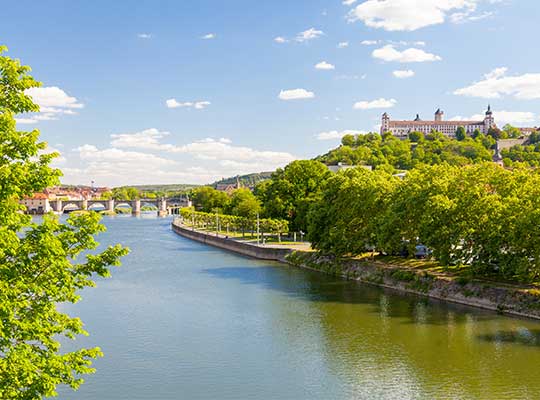 Flusslauf mit Bäumen am Ufer und Schloss im Hintergrund