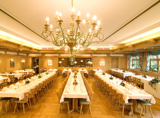 Großer und wunderschöner Saal mit langen Tafeln, die geschmückt sind mit weißen Tischdecken in gemütlichem Ambiente