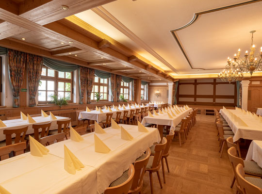 Rustikaler und moderner Saal mit langen Tischreihen und drapierten Servietten unter großen Kronleuchtern