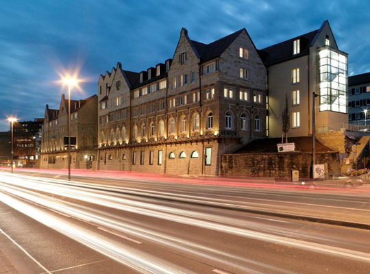 Ansicht des Arcotel Camino über die Straße und am Abend fotografiert mit leuchtenden Laternen und Fenstern