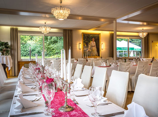 Schön dekorierter Speisesaal mit langen Tafeln und weißen Tischdecken, Stühle sind in Hussen gehüllt und pinke Tischläufer liegen auf dem Tisch
