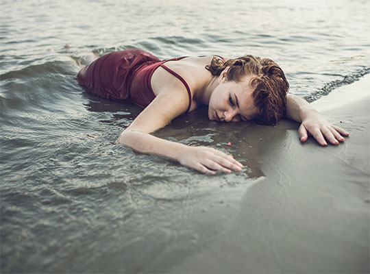 Eine Frau in einem roten Kleid liegt bewusstlos im Meer