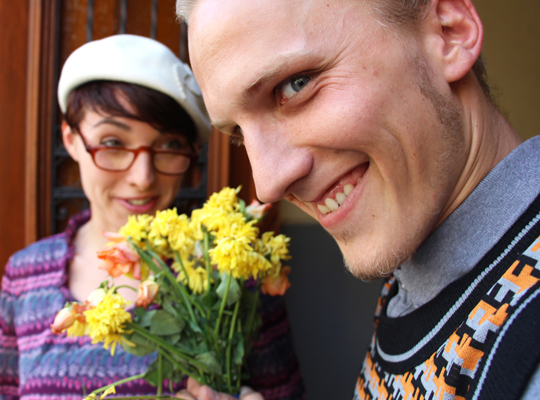 Ein Mann mit Blumenstrauß und verzogenem Gesicht wird schief von einer Frau angeschaut.