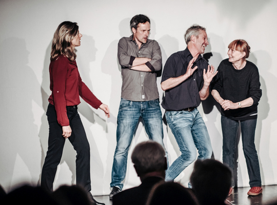 Vier Schauspieler/innen machen verschiedene Grimmassen auf der Bühne.