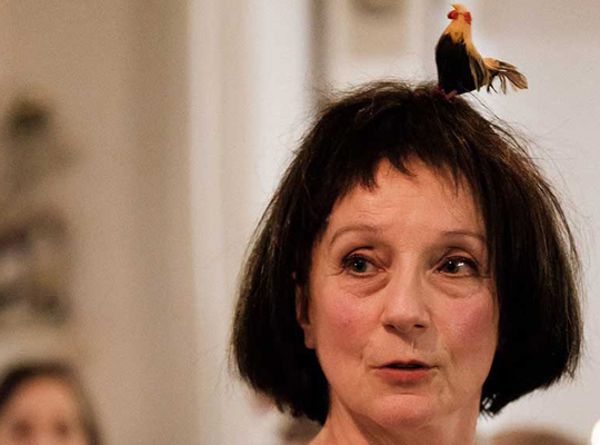 Ein bunter Vogel sitzt auf dem Kopf einer Frau, die es kaum zu merken scheint.