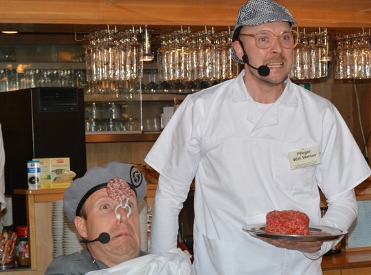 Ein Mann serviert einen schmackhaften Teller Mett an eine sitzende Person mit Nasenklammer.