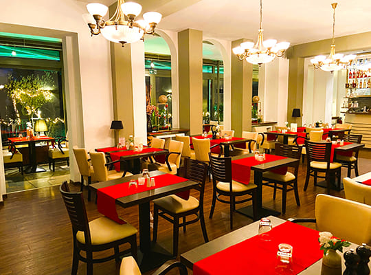 Hochmoderner Restaurantbereich mit bequemen Sitzmöbeln, traumhaften Deckenleuchten und Blick auf die schön beleuchtete Terasse.