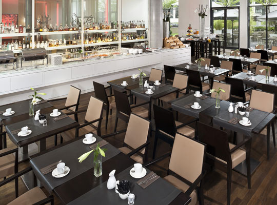 Restaurant, modern, schwarze Tische und hellbraune Stühle, Frühstücksbuffet im Hintergrund