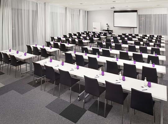 Großer Konferenzsaal mit neumodischem Teppichboden und vielen Sitzreihen.