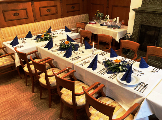 Charmant gedeckte Tischtafel mit weißer Tischdecke, blauen Servietten und bequemen Polsterstühlen. Im Hintergrund ein wunderschöner alter Kamin.
