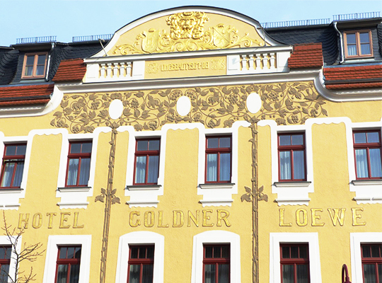 Goldene Außenfassade, mit dem Schriftzug "Hotel Goldner Loewe" und einem Wappen auf der Dach Empore.