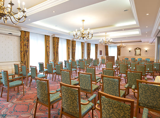 Großer Besprechungssaal bestuhlt mit grünen, gepolsterten Stühlen und schönen Deckenleuchten.