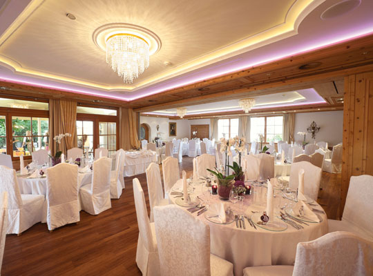 Festlich geschmückter Saal mit hochwertigem Holzboden, weißen Stühlen und Lichtakzenten