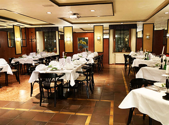 Durch Wandlampen schön beleuchteter Essenssaal. Weiß gedeckte Tischen auf glänzen gefliestem Boden.
