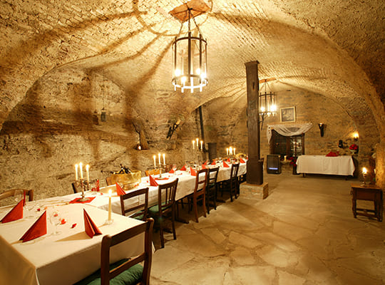 Lange Tischtafel im Gewölbekeller des Restaurants mit schöner beigen Steinmauer und heller Beleuchtung.