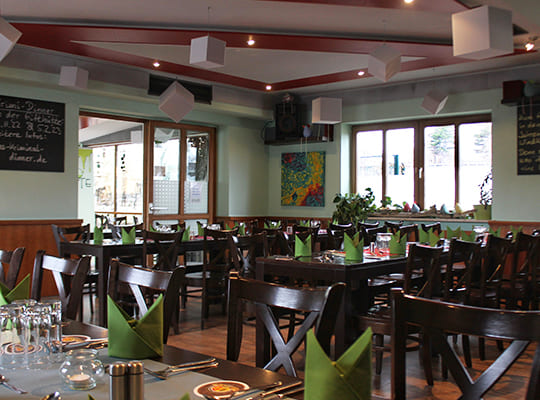 Liebevoll eingerichteter Speisesaal mit grünen Servietten und türkieser Wandfarbe kombiniert mit Holzfarben.