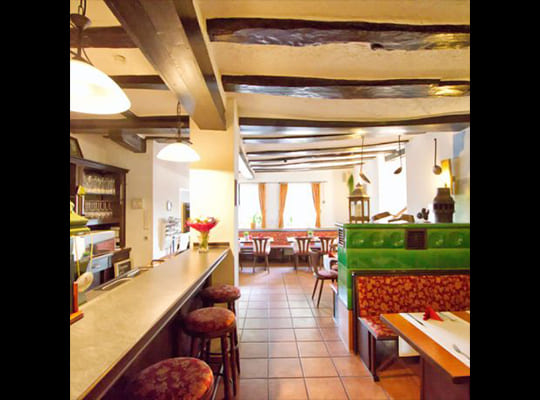 Altmödischer aber schön eingerichteter Restaurantbereich mit vielen gemütlichen Sitzgelegenheiten und einem alten, grünen Kachelofen sowie einer schönen Bar/Theke
