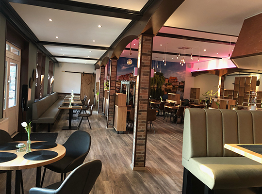 Großer Restaurantsaal, mit vielen bequemen Sitzgelegenheiten, mit Backsteinen verkleidete Säulen und großem Wandbild der Stadt Lüneburg.
