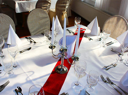 Schön angerichteter Restauranttisch mit weißer Tischdecke, roter Überdeckecke, Besteck und einem schönen Kerzenständer.
