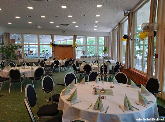 Runder Tisch mit weißer Tischdecke, gefalteten Servietten auf dem Tisch und schwarze Stühle um den Tisch herum
