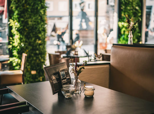 Einladend dekorierter Restaurant-Bereich mit gemütlichen Sitzmöbeln und großen Fensterfronten.